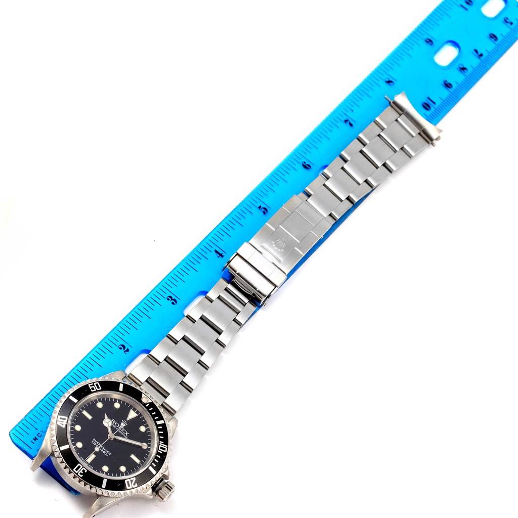 The image shows a Rolex Submariner 14060 Men's Stainless Steel Black Dial 14060 Men's Stainless Steel Black Dial watch lying flat with its stainless steel bracelet extended next to a blue ruler.