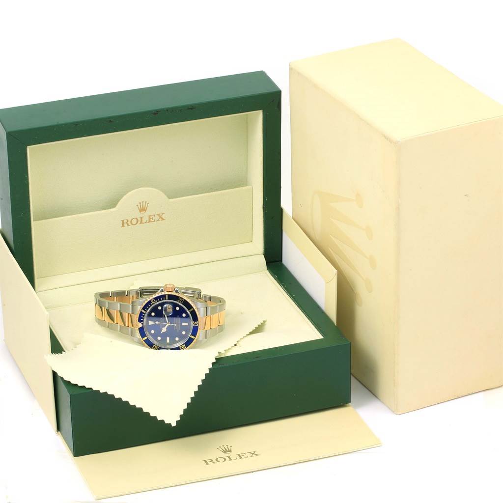 The image shows a Rolex Submariner 16613 Men's Steel and Gold (two tone) Blue Dial 16613 Men's Steel and Gold (two tone) Blue Dial watch in a green display box alongside its outer box and a cleaning cloth.