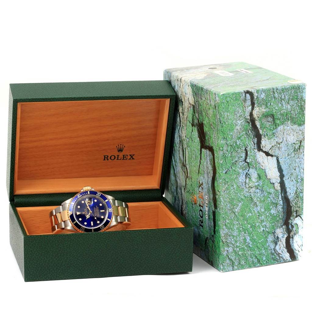 The Rolex Submariner 16613 Men's Steel and Gold (two tone) Blue Dial 16613 Men's Steel and Gold (two tone) Blue Dial watch is shown in its open leather and wooden box with the outer green textured box beside it.