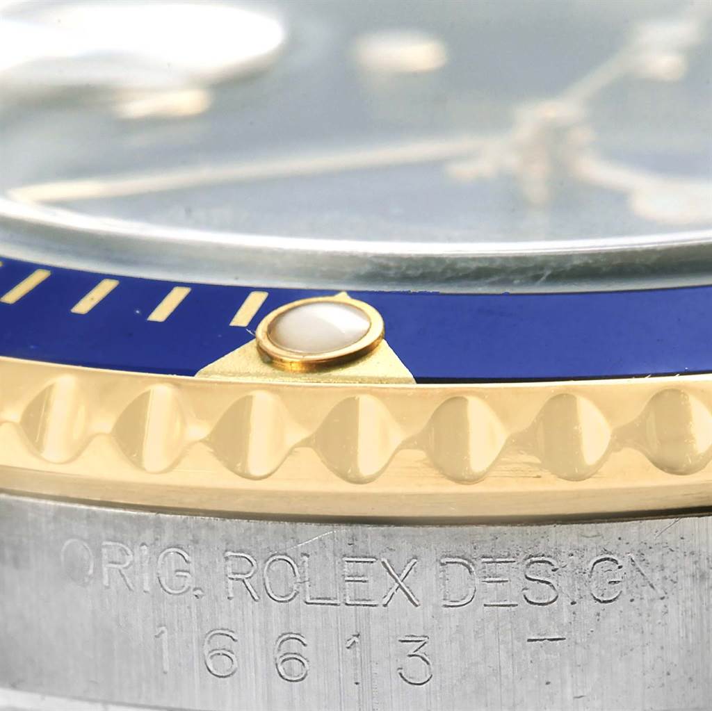 Close-up of a Rolex Submariner 16613 Men's Steel and Gold (two tone) Blue Dial 16613 Men's Steel and Gold (two tone) Blue Dial watch bezel, showing the edge of the dial, blue insert, and text "ORIG. ROLEX DESIGN" with the model number.
