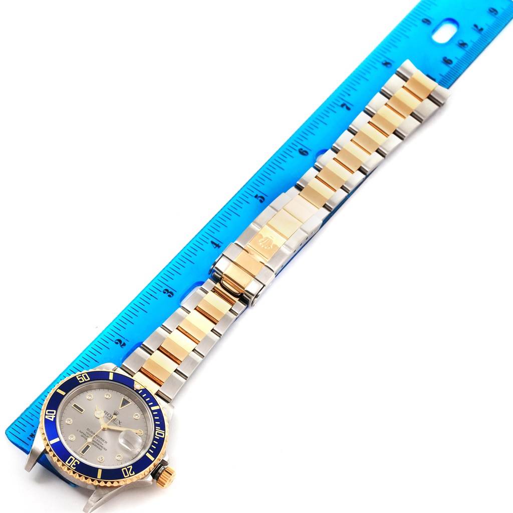 The image shows a Rolex Submariner 16613 Men
s Steel and Gold (two tone) Grey Dial 16613 Men
s Steel and Gold (two tone) Grey Dial watch, focusing on its face, bezel, and bracelet, with a ruler measuring the bracelet length.