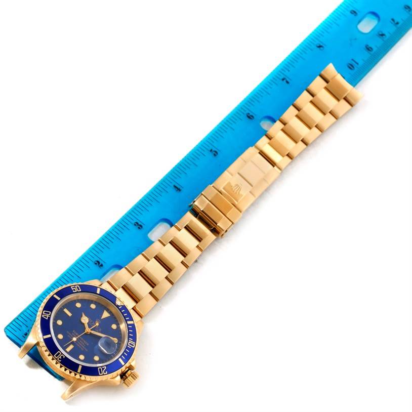 This image shows a Rolex Submariner 16618 Men's Yellow Gold Blue Dial 16618 Men's Yellow Gold Blue Dial watch placed next to a ruler, displaying the face and bracelet at a slight angle.