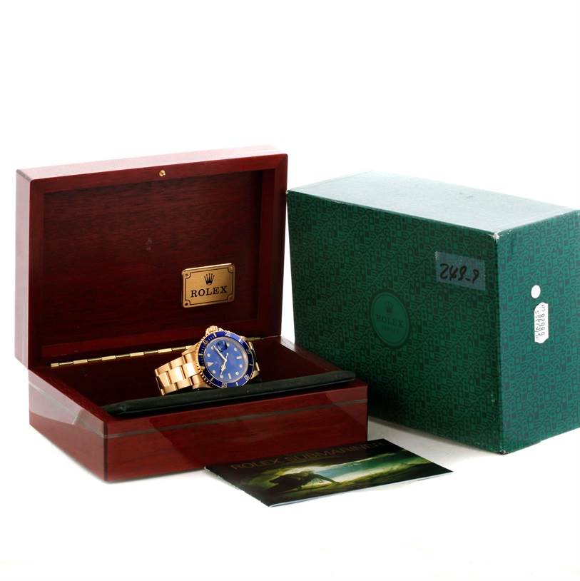 The Rolex Submariner 16618 Men's Yellow Gold Blue Dial 16618 Men's Yellow Gold Blue Dial watch is shown inside its open wooden box, accompanied by its outer green box and some documentation.