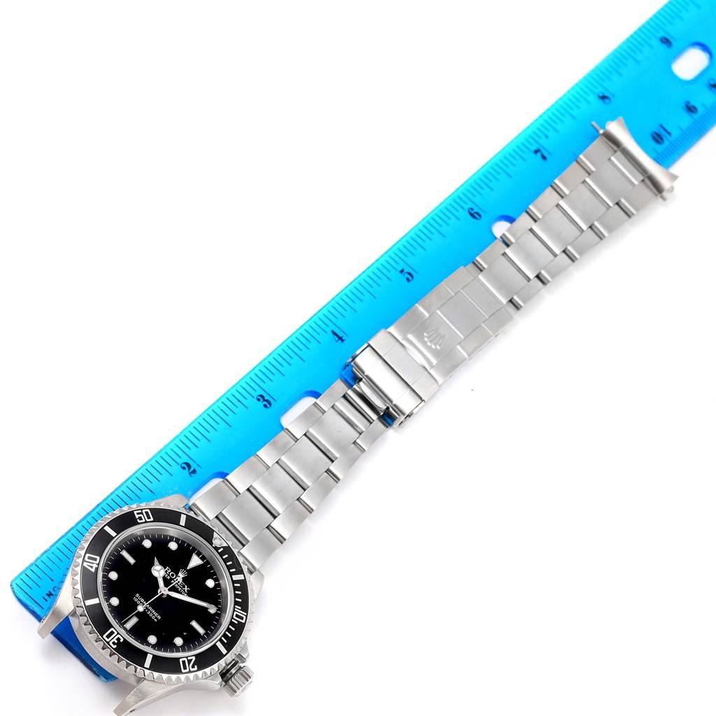 The image shows a top-down view of a Rolex Submariner 14060 Men's Stainless Steel Black Dial 14060 Men's Stainless Steel Black Dial watch with its steel bracelet laid adjacent to a blue ruler.