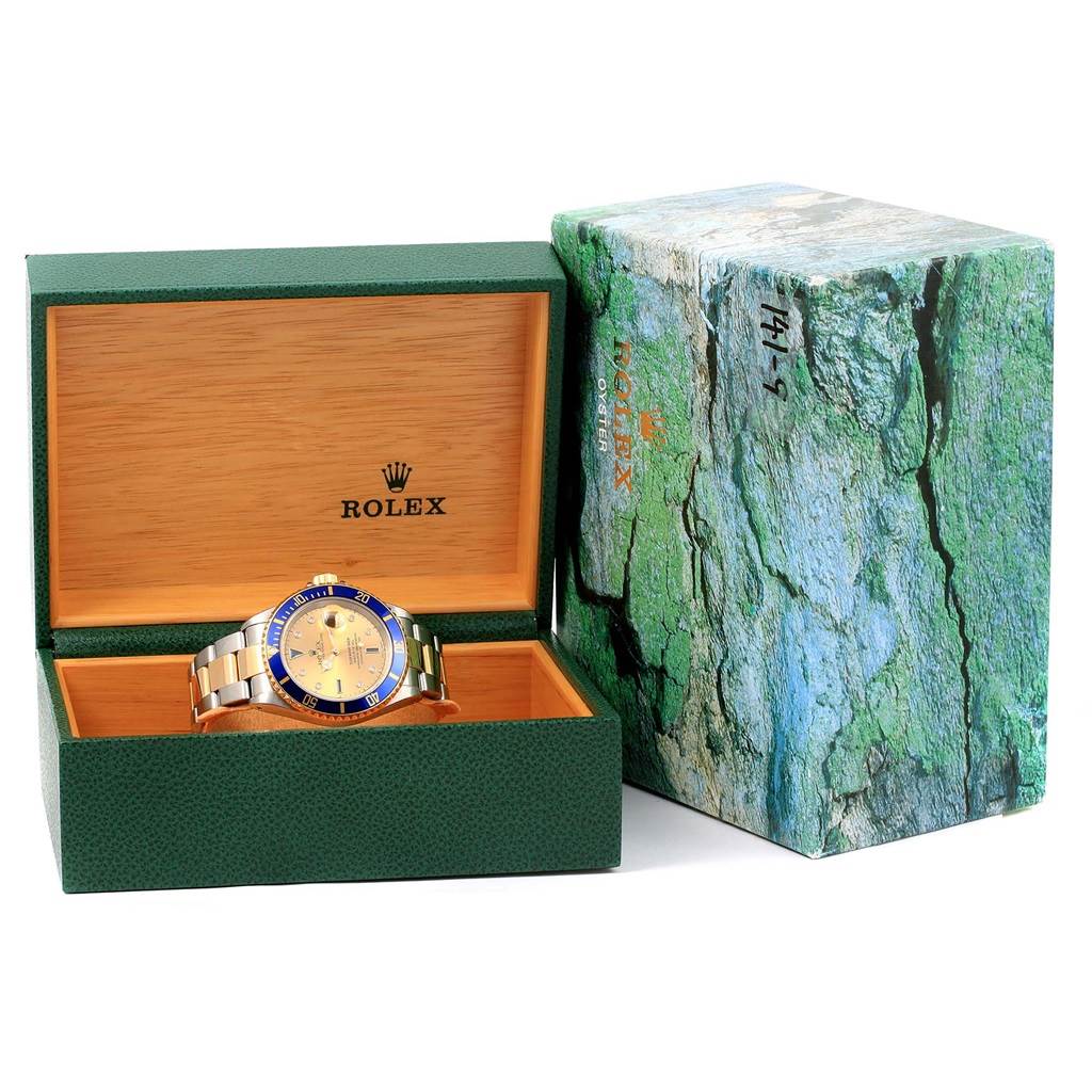 This image shows a Rolex Submariner 16613 Men
s Steel and Gold (two tone) Champagne Dial 16613 Men
s Steel and Gold (two tone) Champagne Dial watch inside an open green and wooden Rolex box with an outer box featuring a textured design.