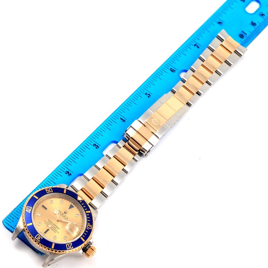 The Rolex Submariner 16613 Men
s Steel and Gold (two tone) Champagne Dial 16613 Men
s Steel and Gold (two tone) Champagne Dial watch is shown from a top-down angle with its blue bezel, gold dial, and two-tone bracelet.