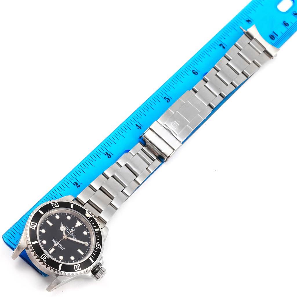 The image shows the front view of a Rolex Submariner 14060 Men
s Stainless Steel Black Dial 14060 Men
s Stainless Steel Black Dial watch lying flat with its stainless steel bracelet and a blue ruler for scale.