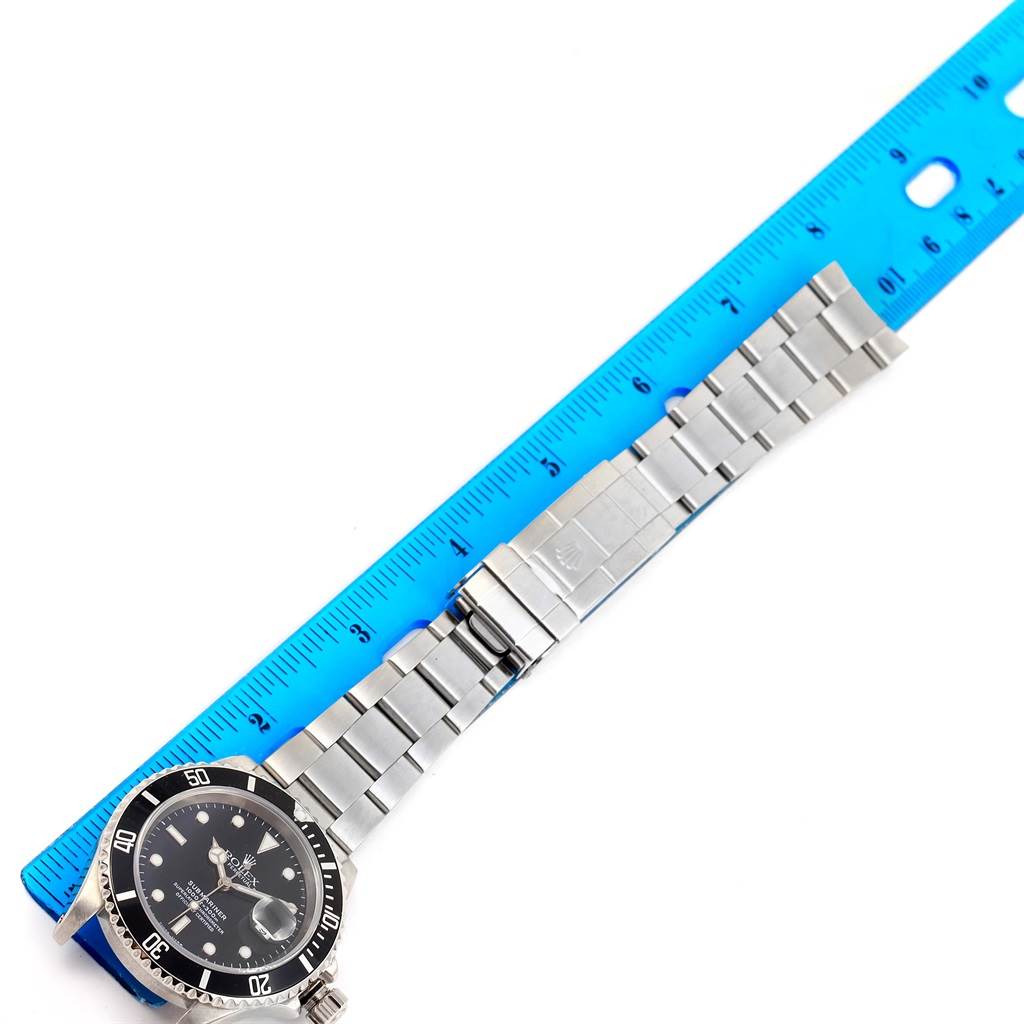 This image shows a Rolex Submariner 16610 Men's Stainless Steel Black Dial 16610 Men's Stainless Steel Black Dial lying flat next to a ruler, displaying the watch face, bracelet, and clasp.
