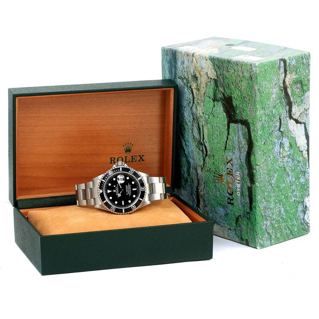 The image shows a Rolex Submariner 16610 Men's Stainless Steel Black Dial 16610 Men's Stainless Steel Black Dial watch in an open box, alongside its green and wooden packaging.