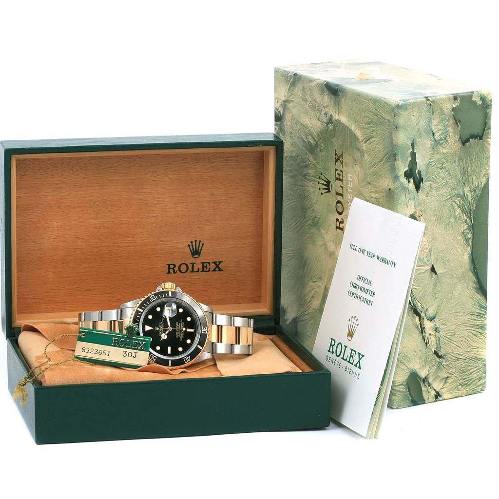 The Rolex Submariner 16803 Men
s Steel and Gold (two tone) Black Dial 16803 Men
s Steel and Gold (two tone) Black Dial watch is displayed in its box with warranty papers and outer packaging visible.