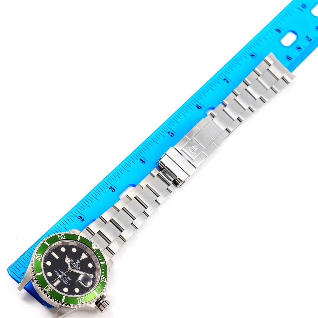 This image shows a Rolex Submariner 16610LV Men's Stainless Steel Black Dial 16610LV Men's Stainless Steel Black Dial watch and its stainless steel bracelet laid flat next to a ruler.