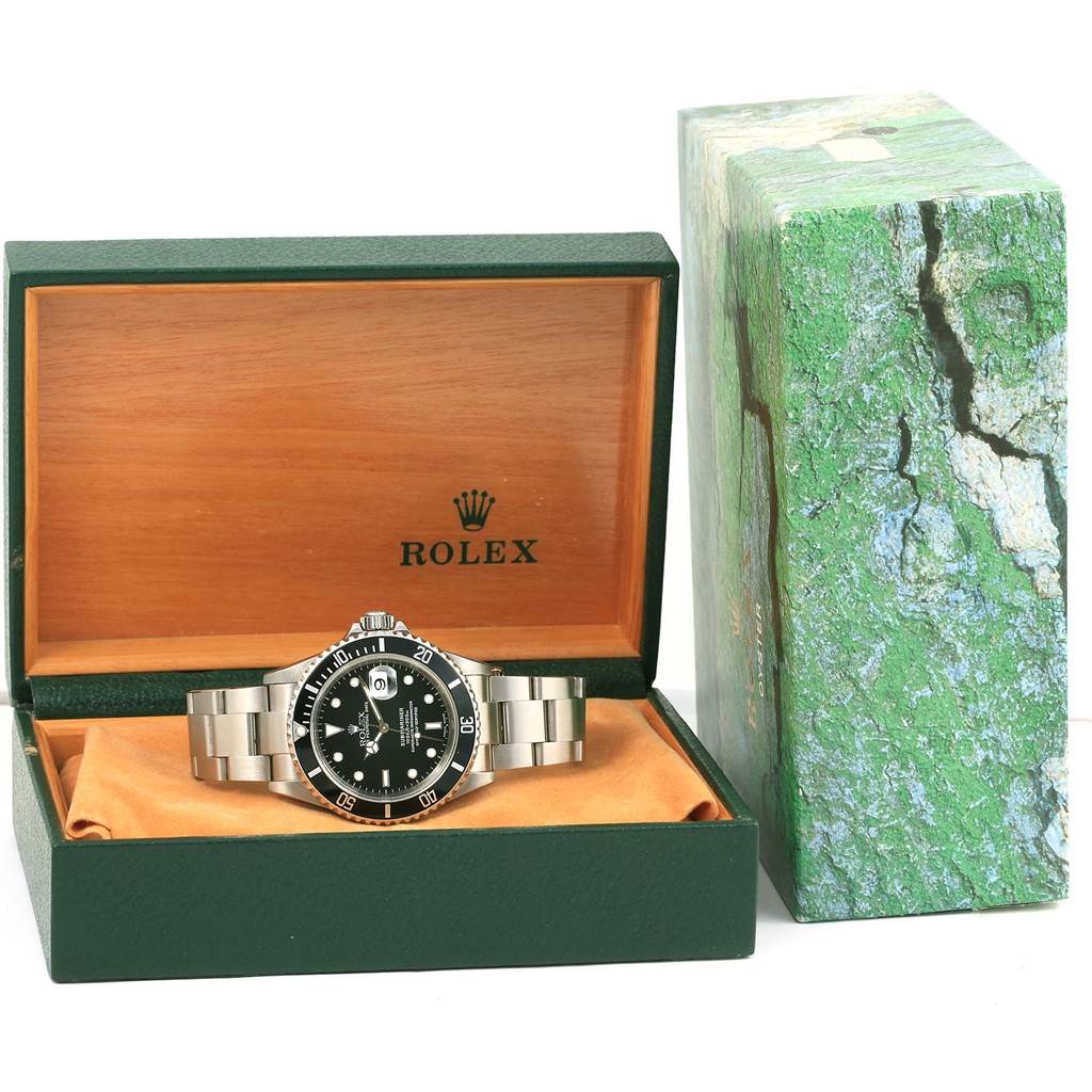 The Rolex Submariner 16610 Men's Stainless Steel Black Dial 16610 Men's Stainless Steel Black Dial watch is displayed in its open box at a frontal angle, with its bracelet laid out and its packaging visible.