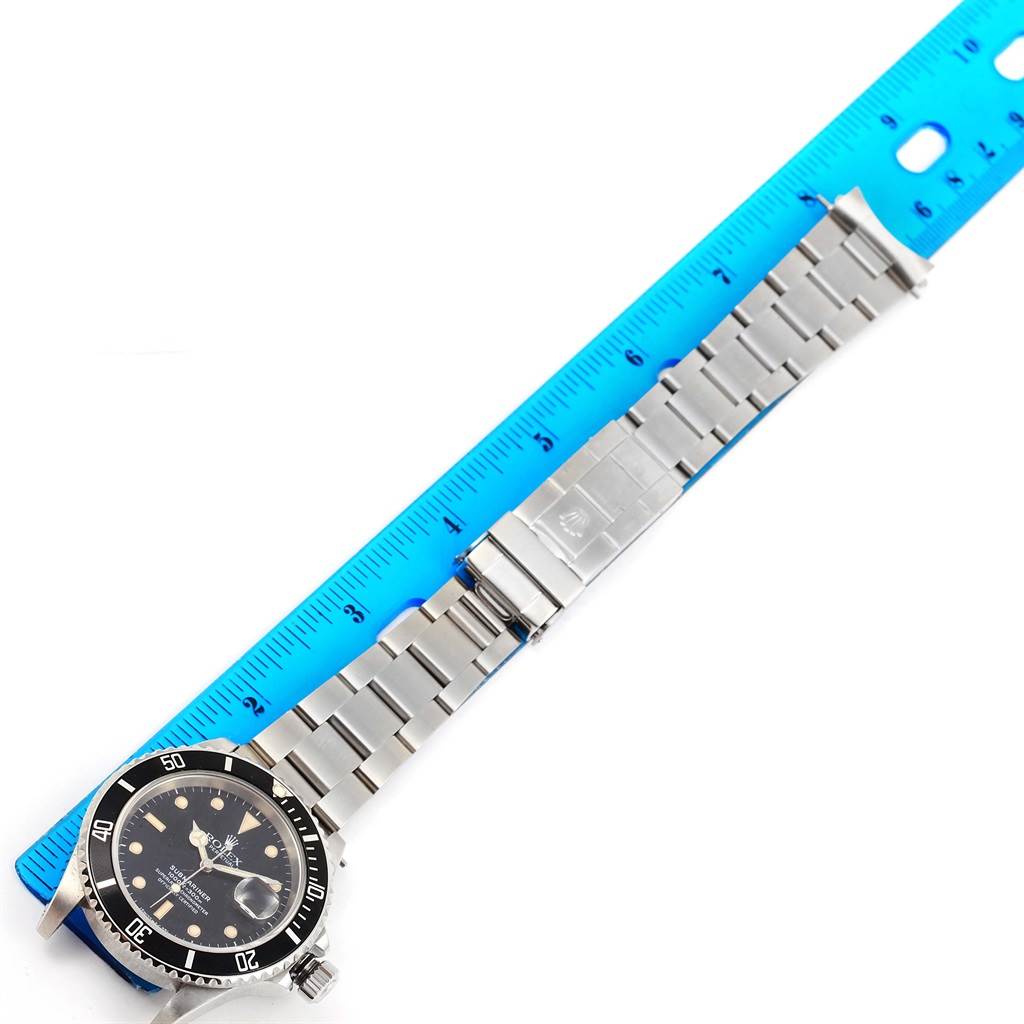 The image shows the side view of a Rolex Submariner 16610 Men's Stainless Steel Black Dial 16610 Men's Stainless Steel Black Dial watch with its metal bracelet laid flat, next to a blue ruler.