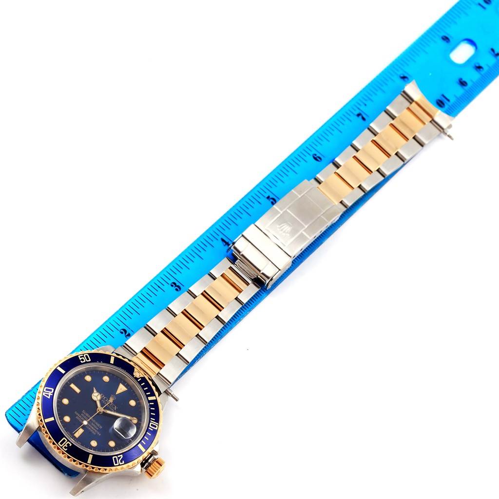 The Rolex Submariner 16803 Men's Steel and Gold (two tone) Blue Dial 16803 Men's Steel and Gold (two tone) Blue Dial watch is shown from a top-down angle, displaying its face, bezel, and metal bracelet next to a blue ruler.