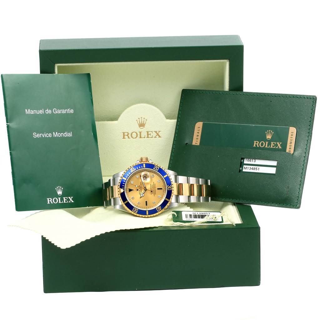 The image shows a Rolex Submariner 16613 Men's Steel and Gold (two tone) Champagne Dial 16613 Men's Steel and Gold (two tone) Champagne Dial with a blue and gold dial, along with manuals and a warranty card in a green box.