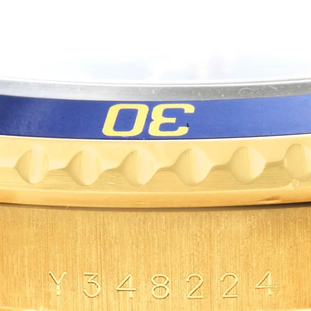 This close-up image of a Rolex Submariner 16618 Men's Yellow Gold Blue Dial 16618 Men's Yellow Gold Blue Dial watch shows the engraved bezel, part of the case, and a serial number.