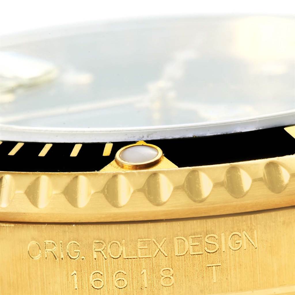This close-up image of a Rolex Submariner 16618 Men's Yellow Gold Black Dial 16618 Men's Yellow Gold Black Dial model shows part of the gold bezel, the edge of the crystal, and engraved text on the case side.