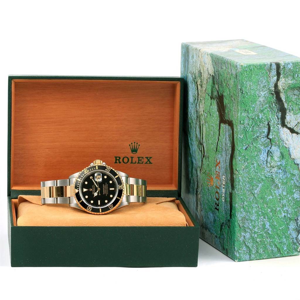 The Rolex Submariner 16613 Men
s Steel and Gold (two tone) Black Dial 16613 Men
s Steel and Gold (two tone) Black Dial watch is displayed head-on in an open box with its outer box nearby.