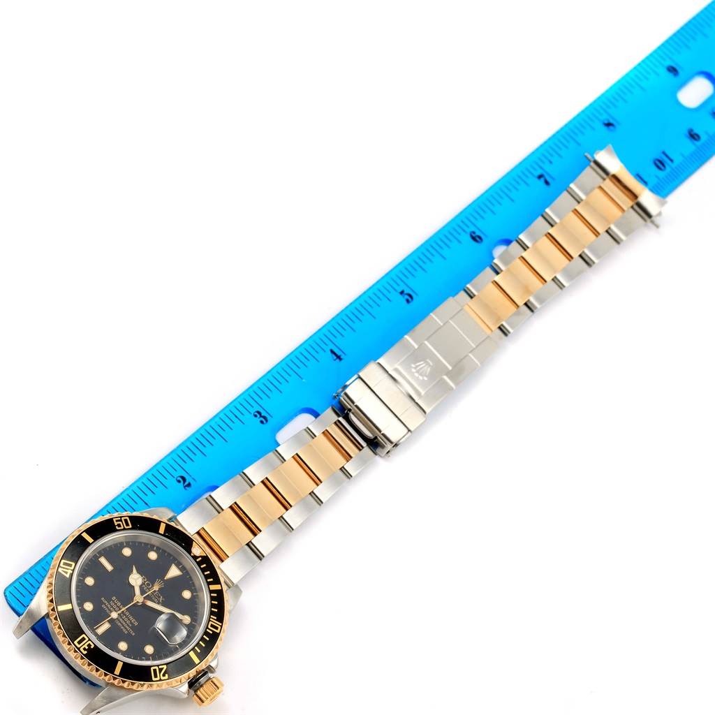 This is a top view of a Rolex Submariner 16613 Men
s Steel and Gold (two tone) Black Dial 16613 Men
s Steel and Gold (two tone) Black Dial watch showing the dial, bezel, and the unfastened bracelet alongside a measuring ruler.