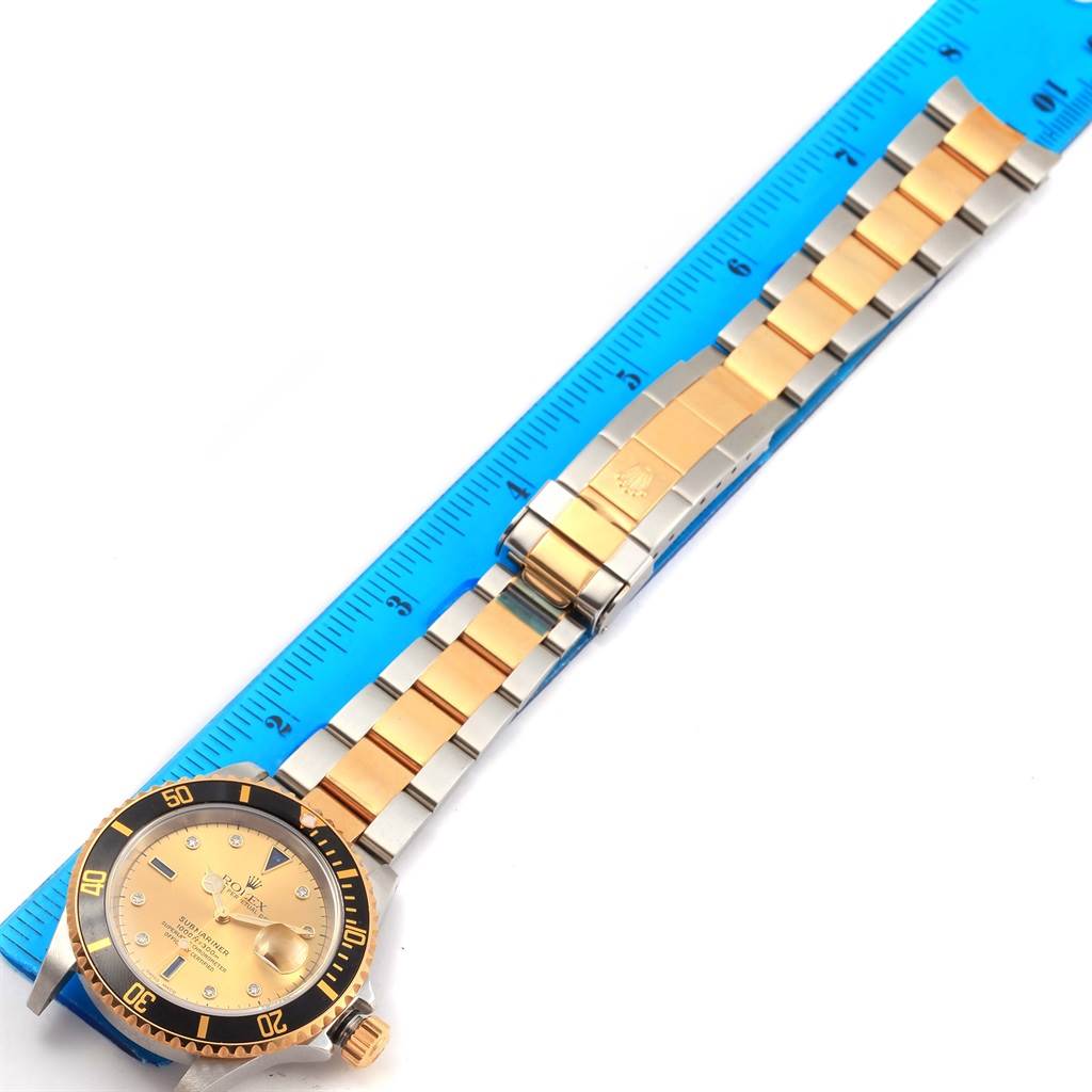 This image shows a full-view of the Rolex Submariner 16613 Men's Steel and Gold (two tone) Champagne Dial 16613 Men's Steel and Gold (two tone) Champagne Dial watch, featuring its gold and silver bracelet and positioned next to a blue ruler.