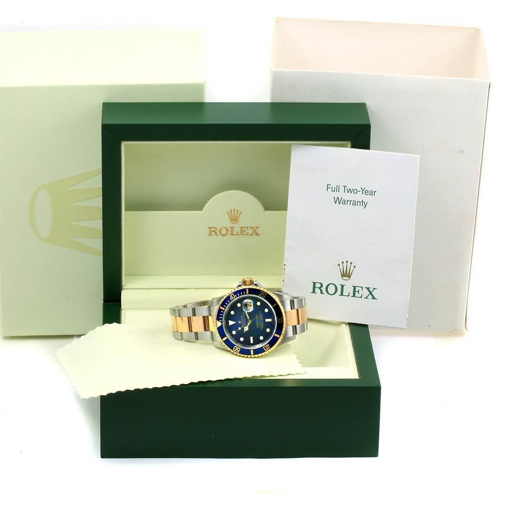 The Rolex Submariner 16613 Men's Steel and Gold (two tone) Blue Dial 16613 Men's Steel and Gold (two tone) Blue Dial watch is displayed in its open green box, with the warranty card and packaging visible in the background.