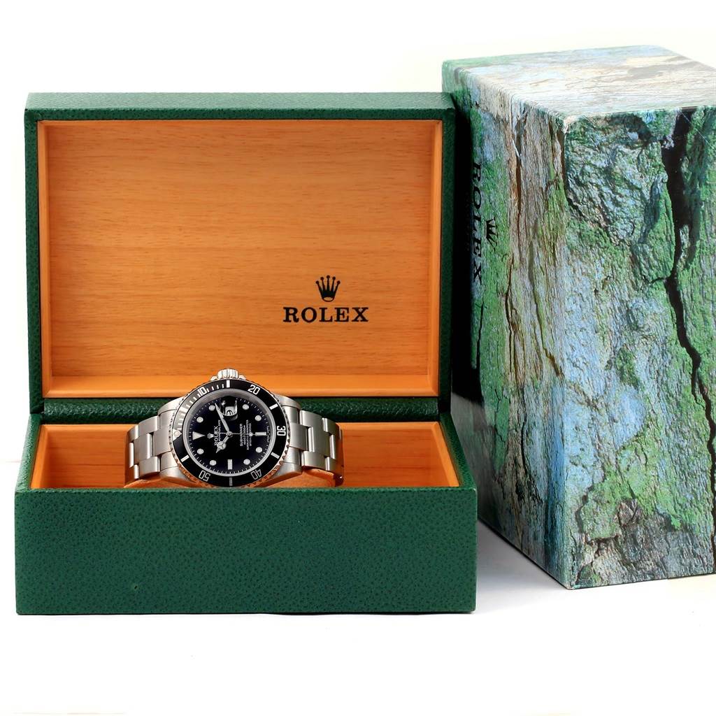 This image displays a Rolex Submariner 16610 Men's Stainless Steel Black Dial 16610 Men's Stainless Steel Black Dial watch positioned in an open green and wooden Rolex box, situated next to the outer packaging.