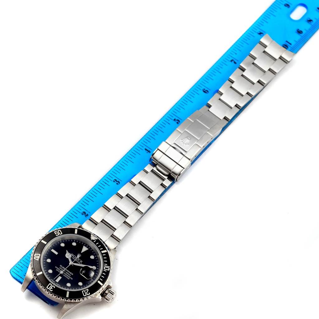 The image shows a Rolex Submariner 16610 Men's Stainless Steel Black Dial 16610 Men's Stainless Steel Black Dial watch laid flat with its stainless steel bracelet next to a ruler for scale measurements.