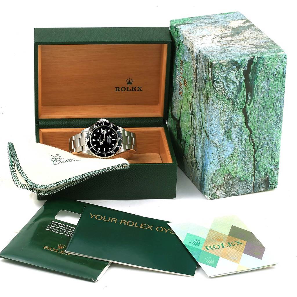 The image shows a Rolex Submariner 16610 Men's Stainless Steel Black Dial 16610 Men's Stainless Steel Black Dial watch in an open box, with accompanying booklets, a cloth, and the exterior box nearby.
