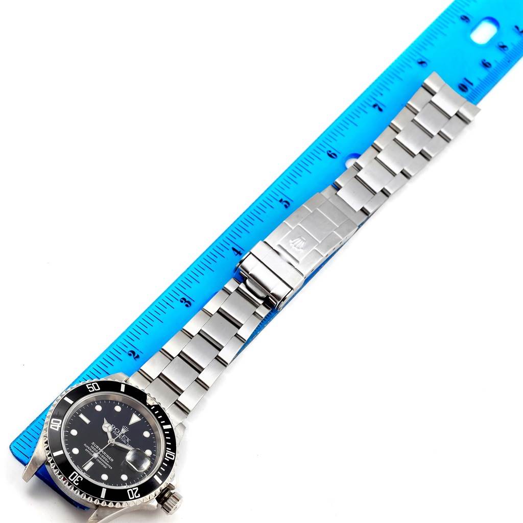 The image shows a Rolex Submariner 16610 Men's Stainless Steel Black Dial 16610 Men's Stainless Steel Black Dial watch laid flat next to a blue ruler, displaying its face and metal bracelet.