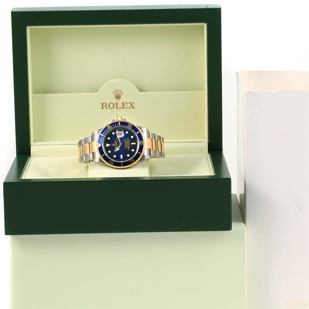 The Rolex Submariner 16613 Men's Steel and Gold (two tone) Blue Dial 16613 Men's Steel and Gold (two tone) Blue Dial watch is displayed front and center in an open green watch box, showing its face and bracelet.