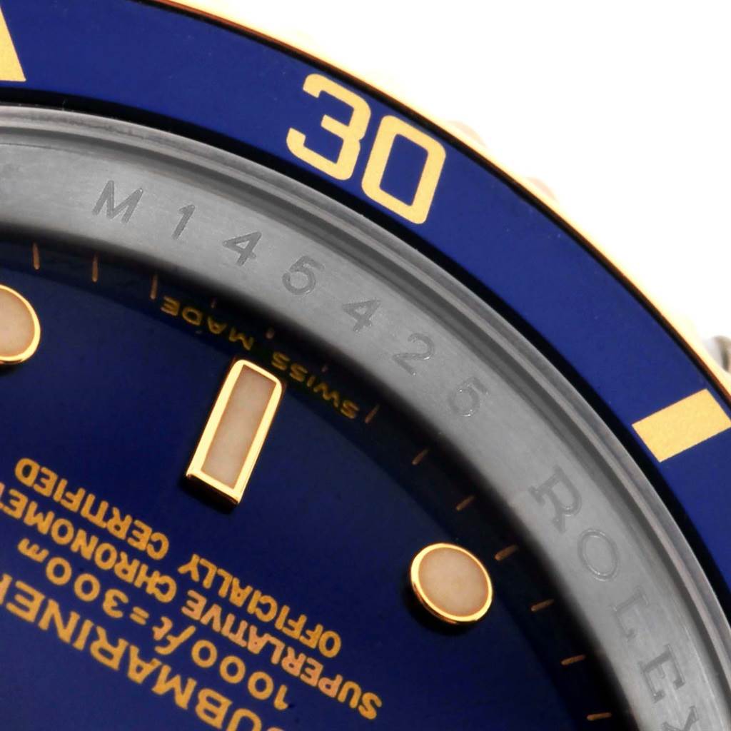 Close-up of the Rolex Submariner 16613 Men's Steel and Gold (two tone) Blue Dial 16613 Men's Steel and Gold (two tone) Blue Dial watch showing part of the blue dial, bezel, and inscriptions, focused on the 30-minute mark and text details.
