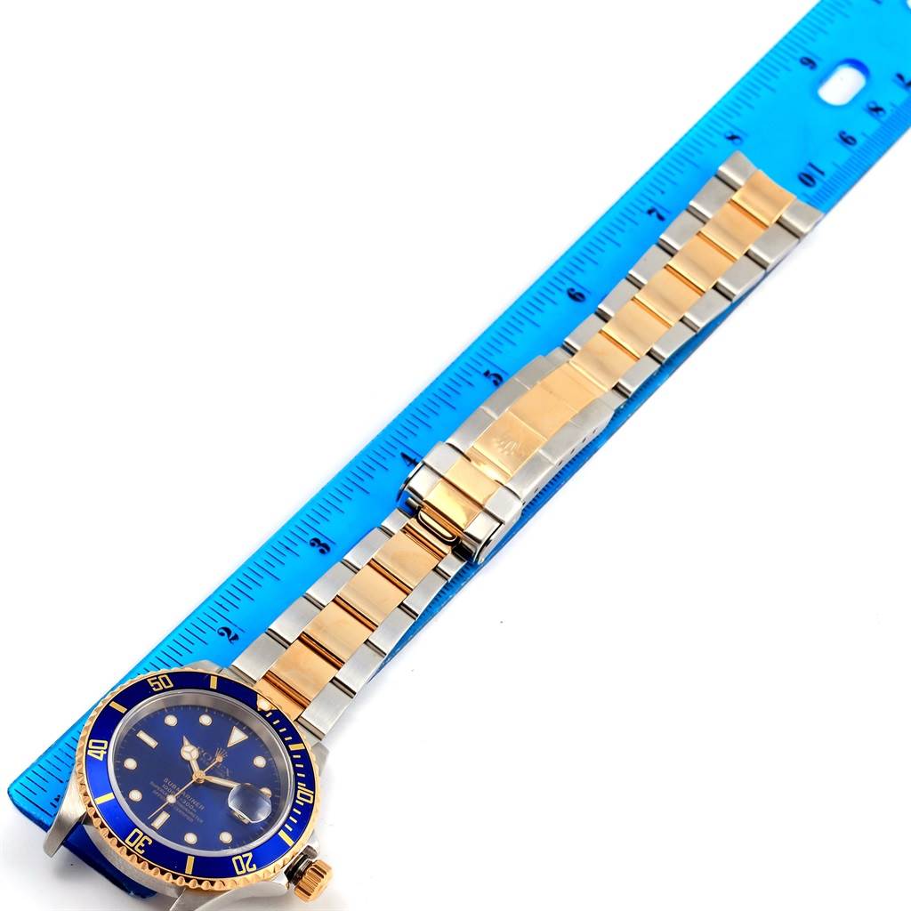The image shows a top-down view of a Rolex Submariner 16613 Men's Steel and Gold (two tone) Blue Dial 16613 Men's Steel and Gold (two tone) Blue Dial watch, including its blue dial, bezel, and two-tone bracelet next to a ruler.