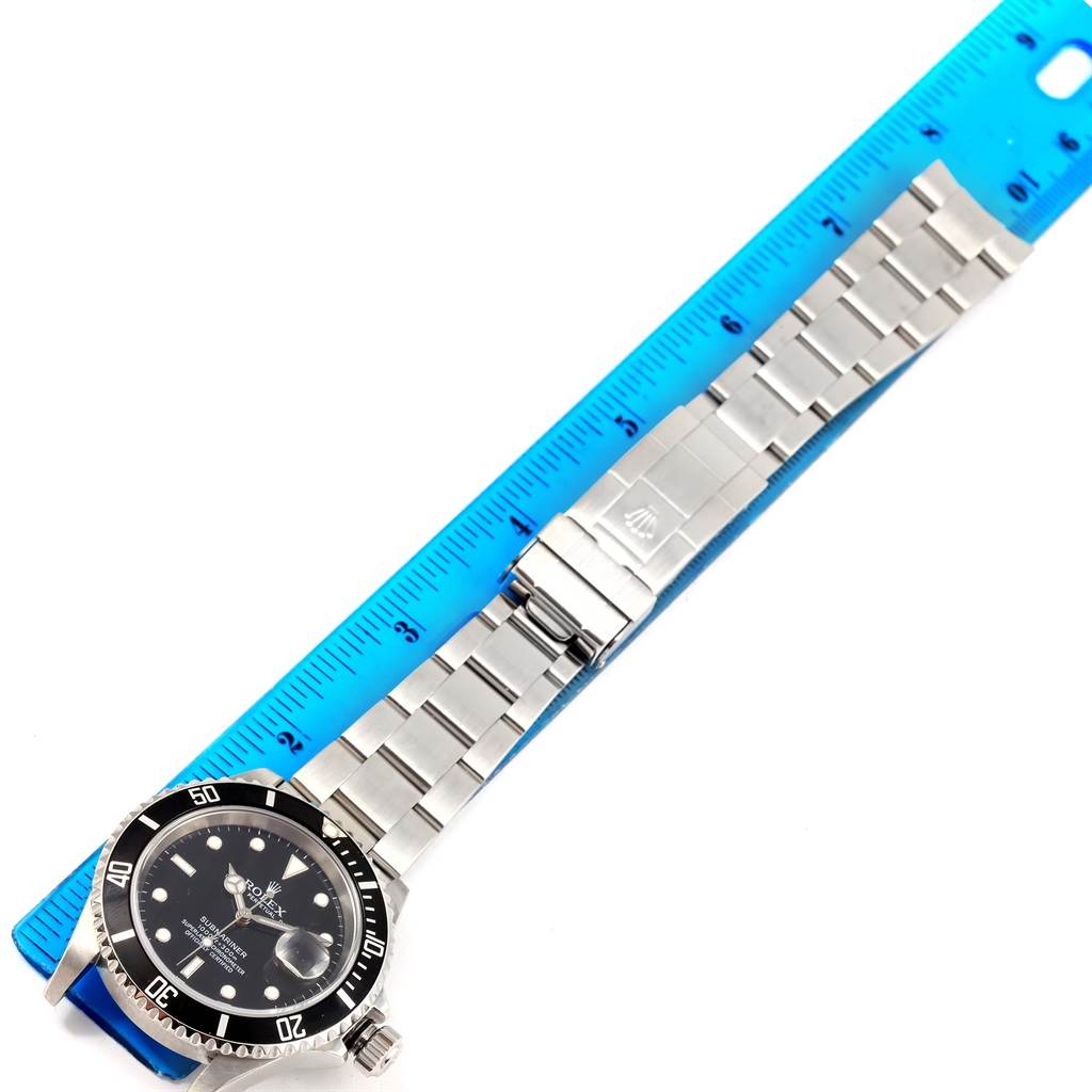 The image shows a top-down view of a Rolex Submariner 16610 Men's Stainless Steel Black Dial 16610 Men's Stainless Steel Black Dial watch with the full length of its band alongside a blue ruler.