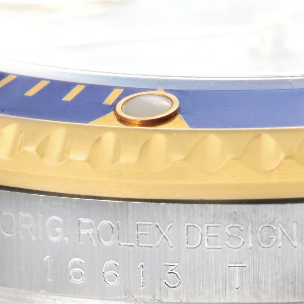 This close-up image of a Rolex Submariner 16613 Men
s Steel and Gold (two tone) Grey Dial 16613 Men
s Steel and Gold (two tone) Grey Dial watch shows parts of the blue and gold bezel, the pearl marker, and "ORIG. ROLEX DESIGN 16613T" engraving.