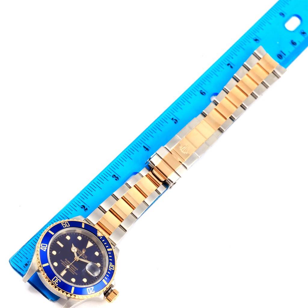 The image shows a Rolex Submariner 16613 Men's Steel and Gold (two tone) Blue Dial 16613 Men's Steel and Gold (two tone) Blue Dial watch laid flat next to a ruler, showcasing the face, bezel, and bracelet.