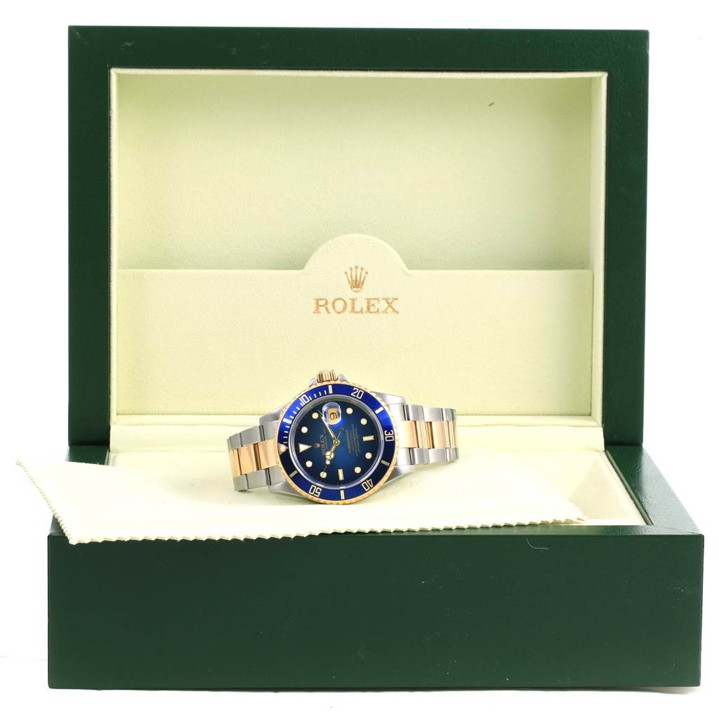 This image shows a Rolex Submariner 16613 Men
s Steel and Gold (two tone) Blue Dial 16613 Men
s Steel and Gold (two tone) Blue Dial watch in its open green box, highlighting the face, bezel, and bracelet of the watch.