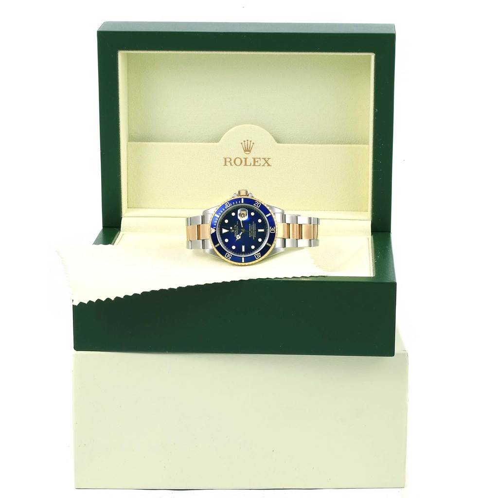 The Rolex Submariner 16613 Men's Steel and Gold (two tone) Blue Dial 16613 Men's Steel and Gold (two tone) Blue Dial watch is displayed head-on inside its green box, with its bracelet partially visible.