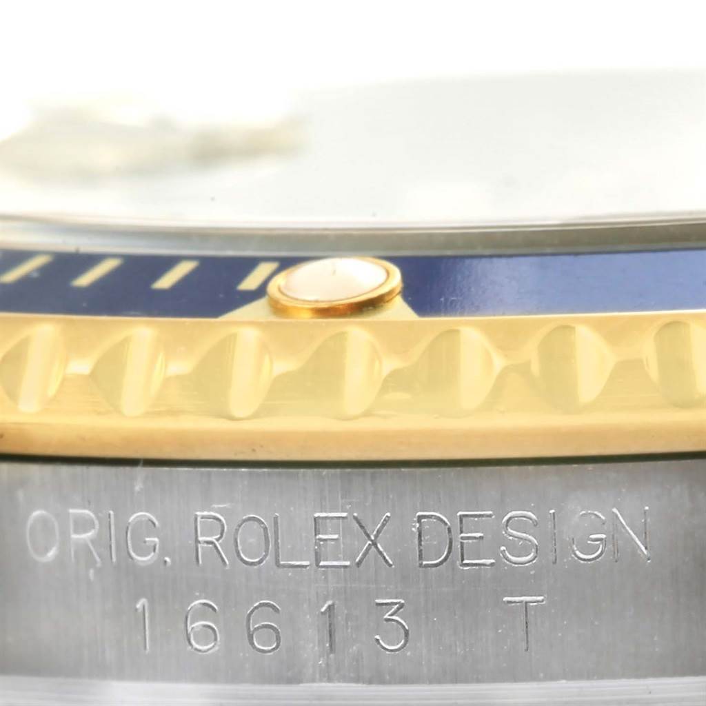 The image shows a close-up of the Rolex Submariner 16613 Men's Steel and Gold (two tone) Blue Dial 16613 Men's Steel and Gold (two tone) Blue Dial's bezel, edge, and the engraved model number 16613 T.