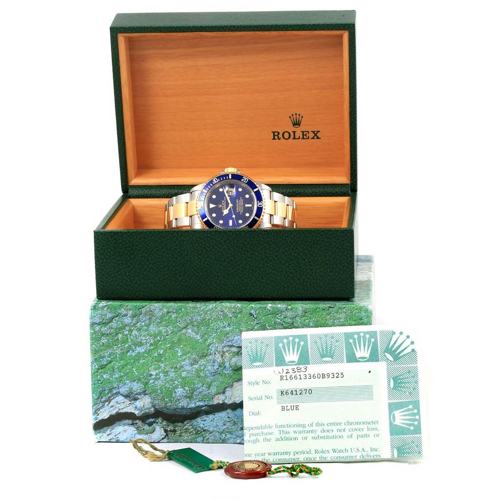 The Rolex Submariner 16613 Men's Steel and Gold (two tone) Blue Dial 16613 Men's Steel and Gold (two tone) Blue Dial watch is shown in an open green box with documentation and tags, angled from the front.