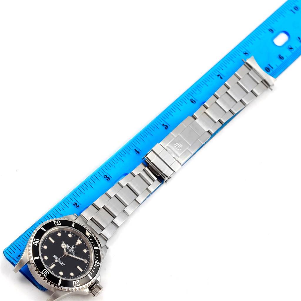 The image shows a Rolex Submariner 14060 Men's Stainless Steel Black Dial 14060 Men's Stainless Steel Black Dial watch laid flat with a blue measuring ruler beside it.
