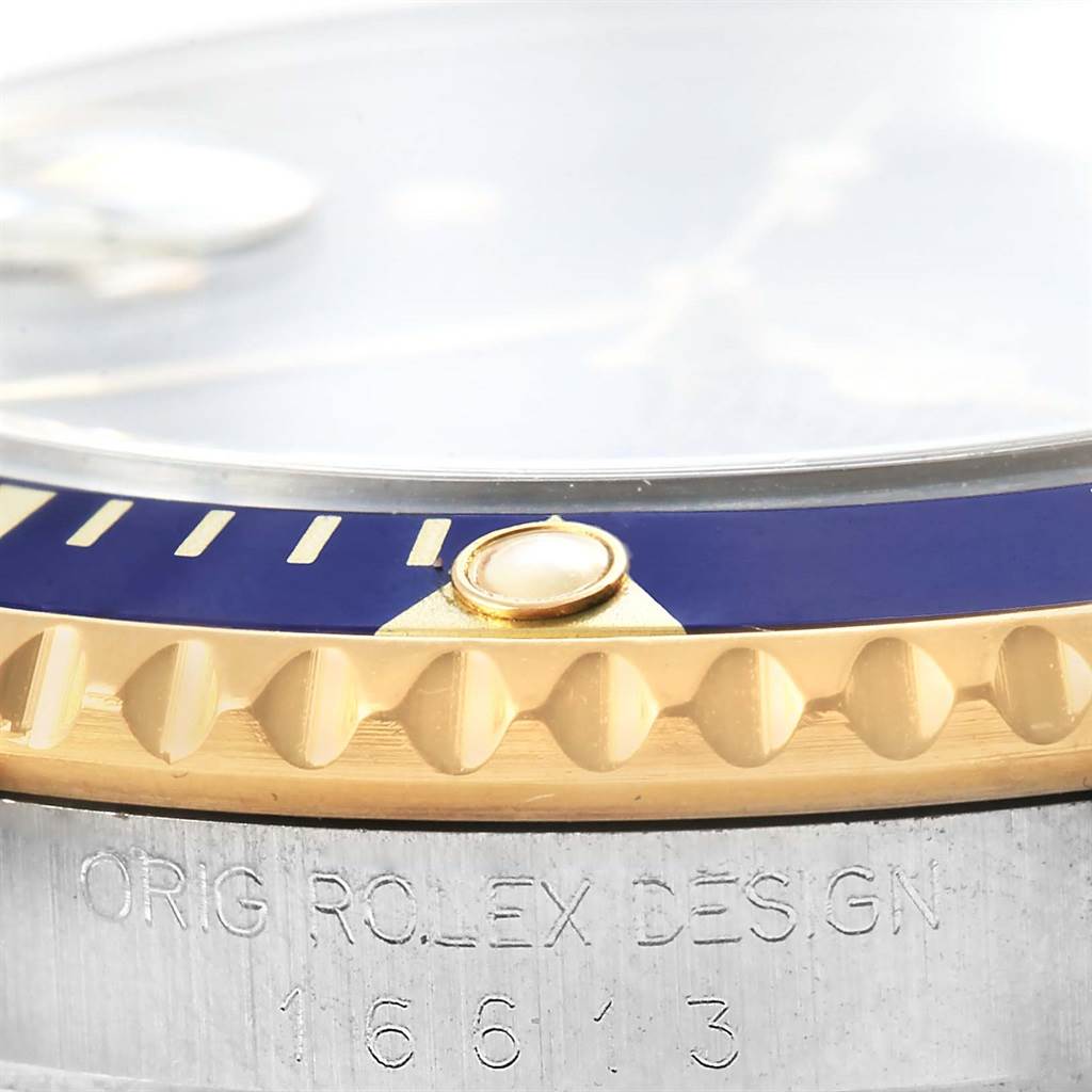 This close-up image of the Rolex Submariner 16613 Men's Steel and Gold (two tone) Blue Dial 16613 Men's Steel and Gold (two tone) Blue Dial watch shows the edge of the bezel, part of the crystal, and the model number engraving 16613.