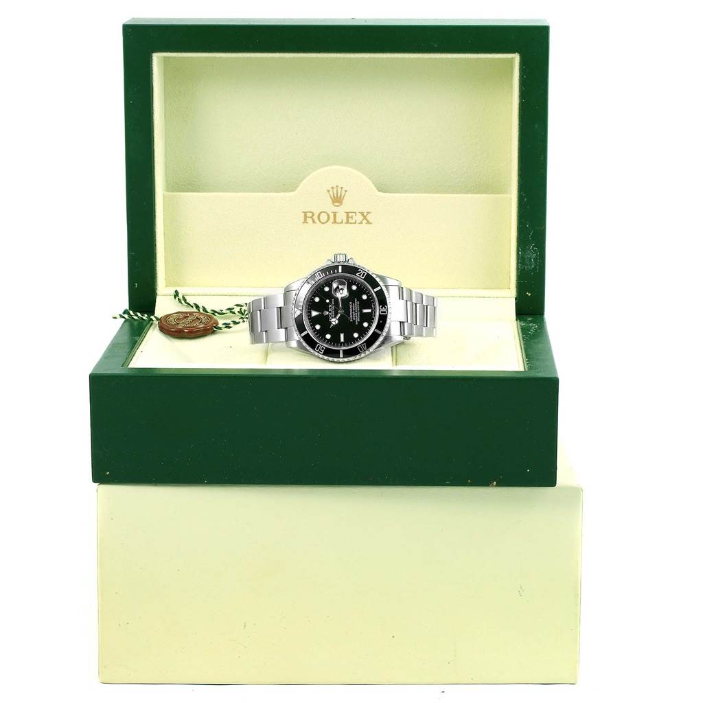 The Rolex Submariner 16610 Men
s Stainless Steel Black Dial 16610 Men
s Stainless Steel Black Dial watch is shown front-facing in an open green Rolex box, alongside a tag.