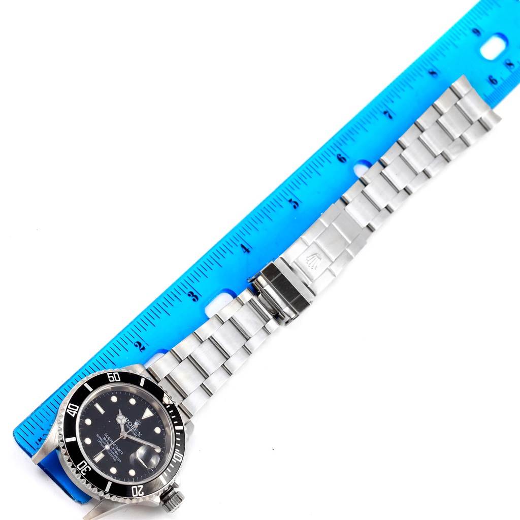 The image shows a Rolex Submariner 16610 Men's Stainless Steel Black Dial 16610 Men's Stainless Steel Black Dial watch placed next to a ruler, highlighting its face, bezel, and bracelet.