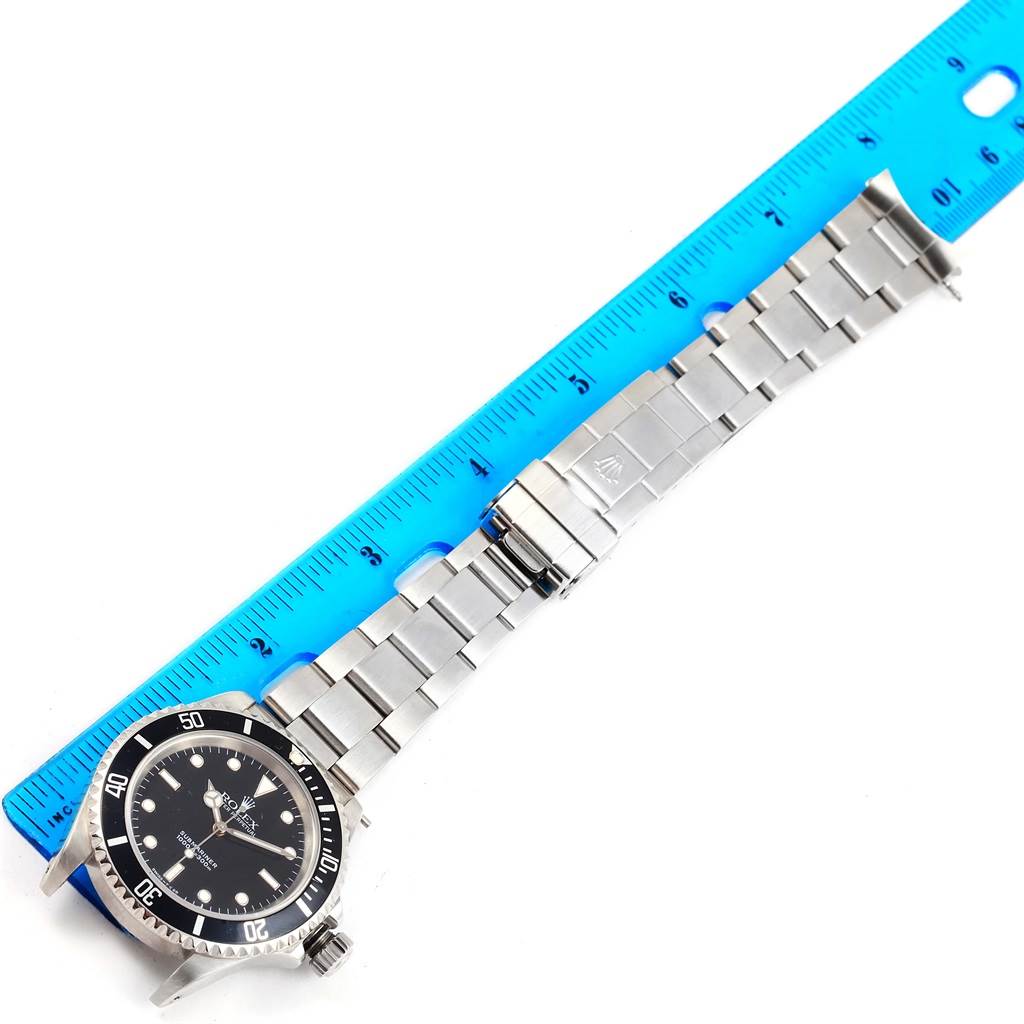 The Rolex Submariner 14060 Men's Stainless Steel Black Dial 14060 Men's Stainless Steel Black Dial watch is shown from an overhead angle, highlighting the face, bezel, and stainless steel bracelet beside a blue ruler.