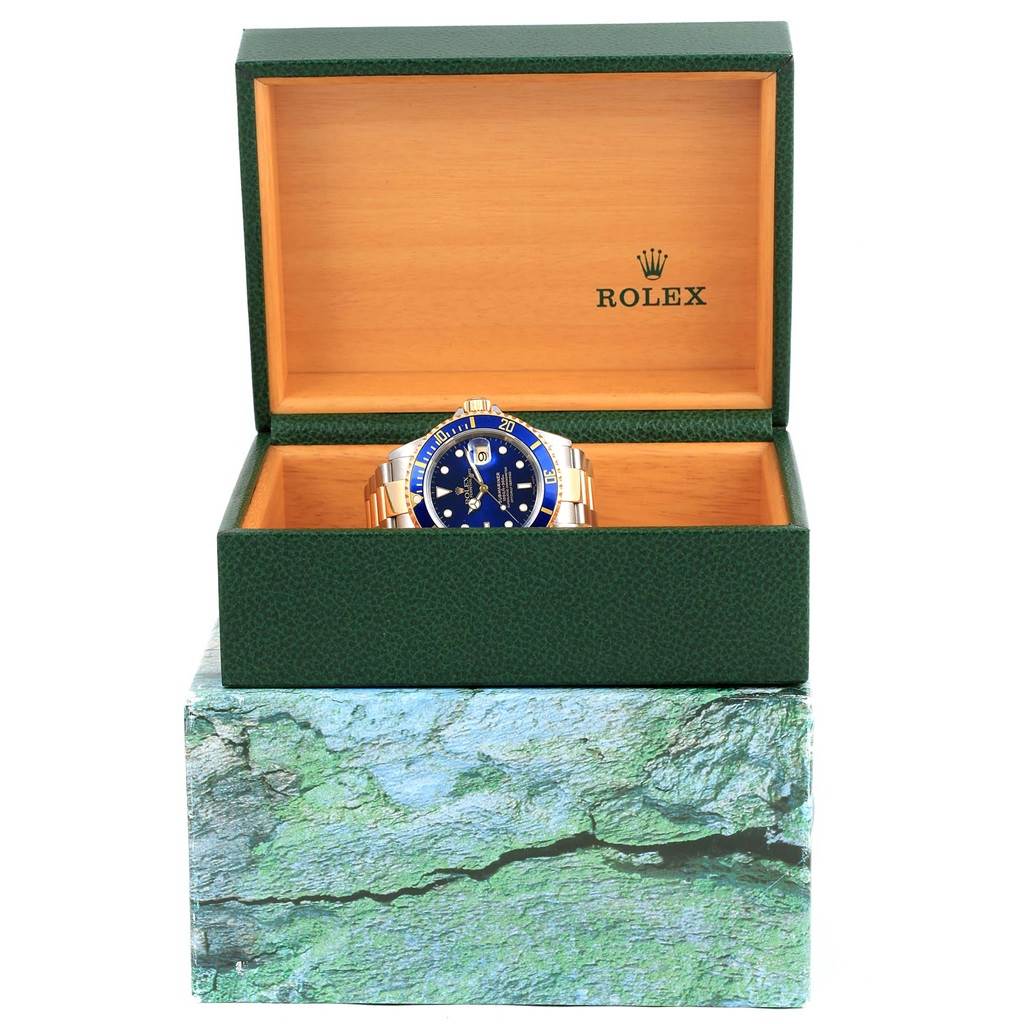 The image displays a Rolex Submariner 16613 Men's Steel and Gold (two tone) Blue Dial 16613 Men's Steel and Gold (two tone) Blue Dial watch placed inside an open green and wooden box, viewed from the front.