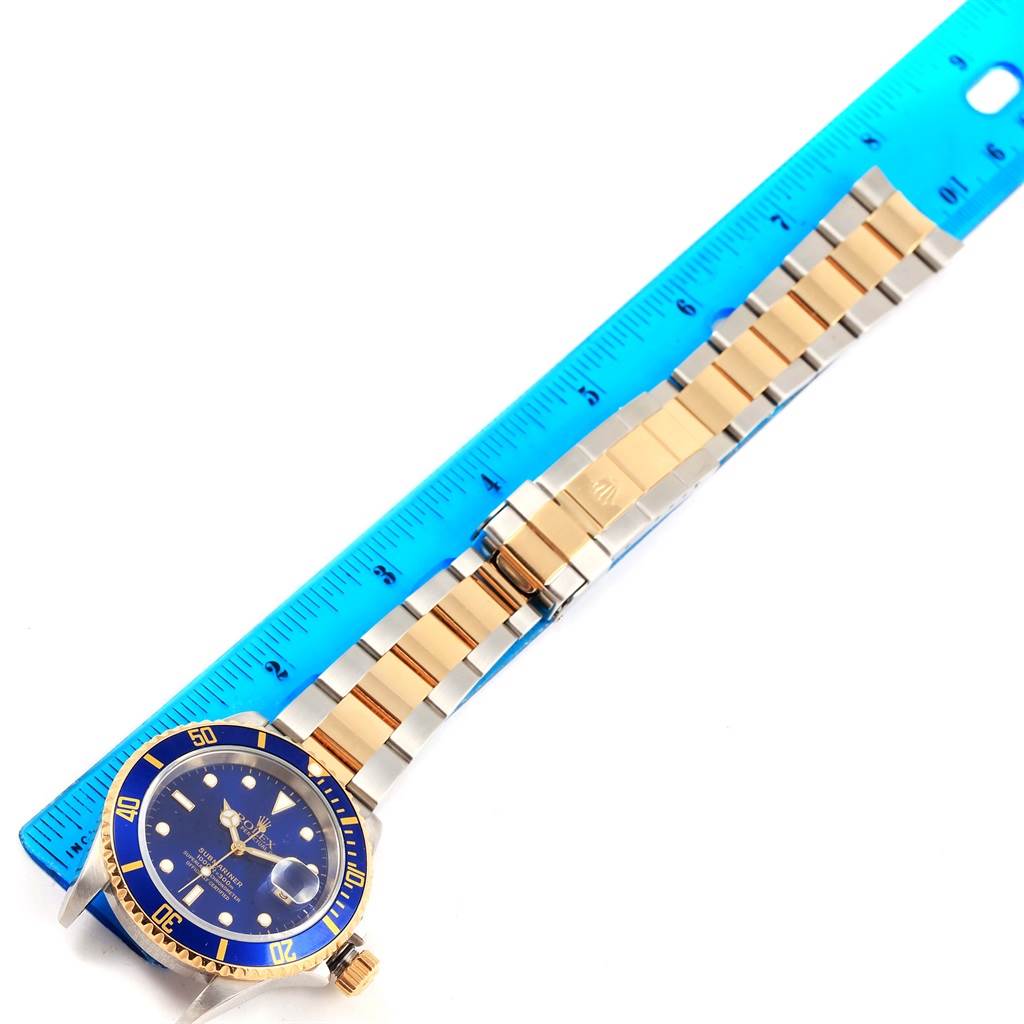 A Rolex Submariner 16613 Men's Steel and Gold (two tone) Blue Dial 16613 Men's Steel and Gold (two tone) Blue Dial watch is shown from an angled view, including the face, bezel, and bracelet, measured against a ruler.