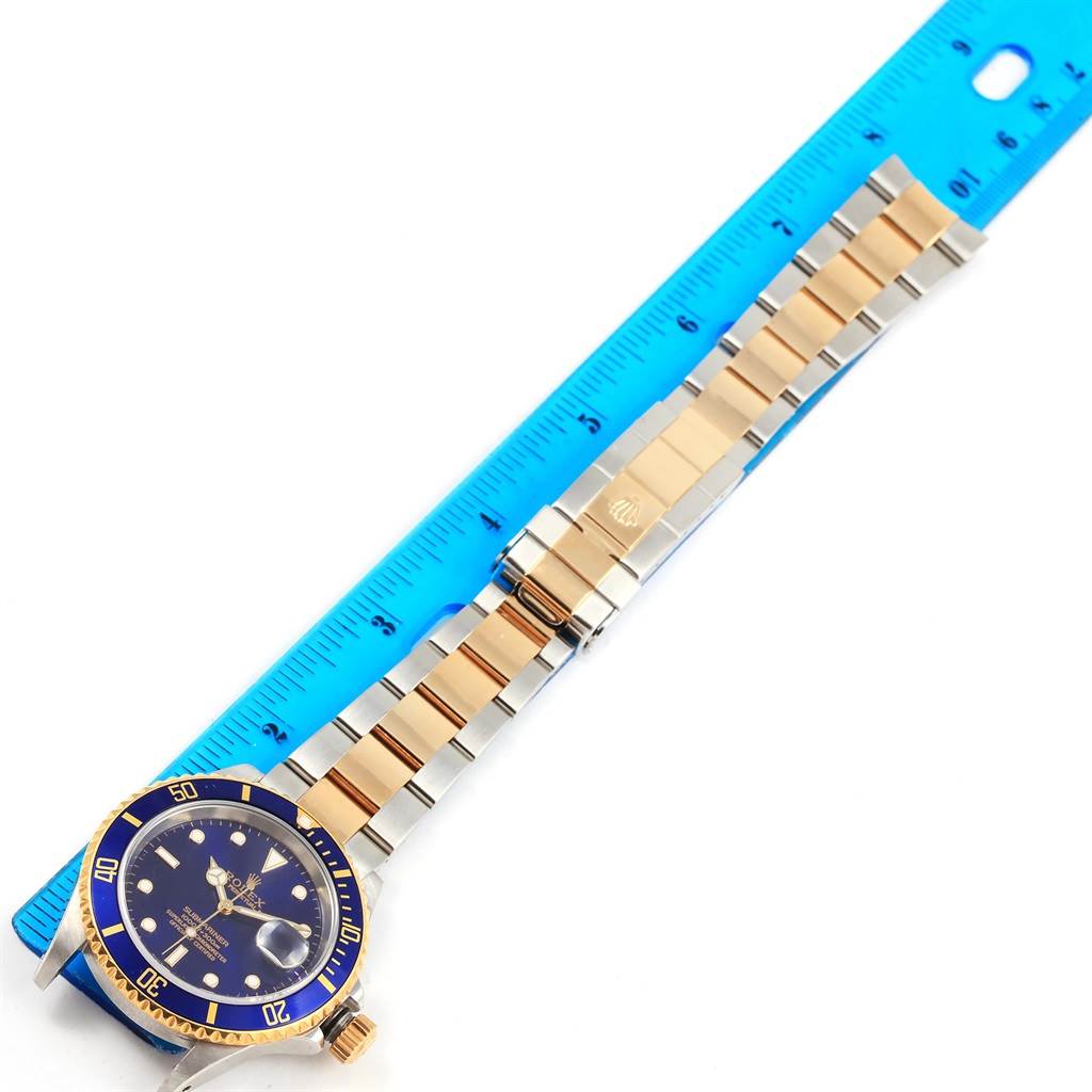 This image shows the front view of a Rolex Submariner 16613 Men's Steel and Gold (two tone) Blue Dial 16613 Men's Steel and Gold (two tone) Blue Dial watch with a blue dial, bezel, and a two-tone bracelet next to a blue ruler.