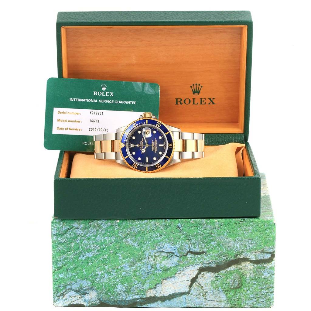 The Rolex Submariner 16613 Men's Steel and Gold (two tone) Blue Dial 16613 Men's Steel and Gold (two tone) Blue Dial watch is shown front-facing inside an open green box, accompanied by an international service guarantee card.