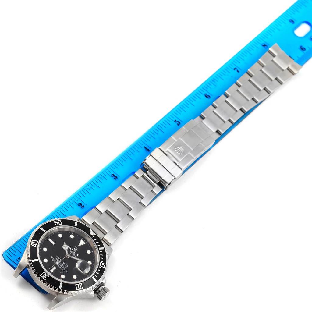 The image shows a Rolex Submariner 16610 Men's Stainless Steel Black Dial 16610 Men's Stainless Steel Black Dial watch laid flat next to a blue ruler, displaying its face and stainless steel band.