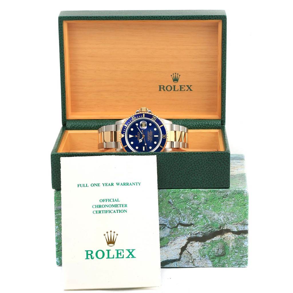 The Rolex Submariner 16803 Men's Steel and Gold (two tone) Blue Dial 16803 Men's Steel and Gold (two tone) Blue Dial watch is displayed frontally in an open green box, accompanied by warranty and certification papers.